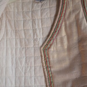 May include: A quilted vest with a white background and a green and red trim. The vest is made of a soft, lightweight fabric and has a relaxed fit.