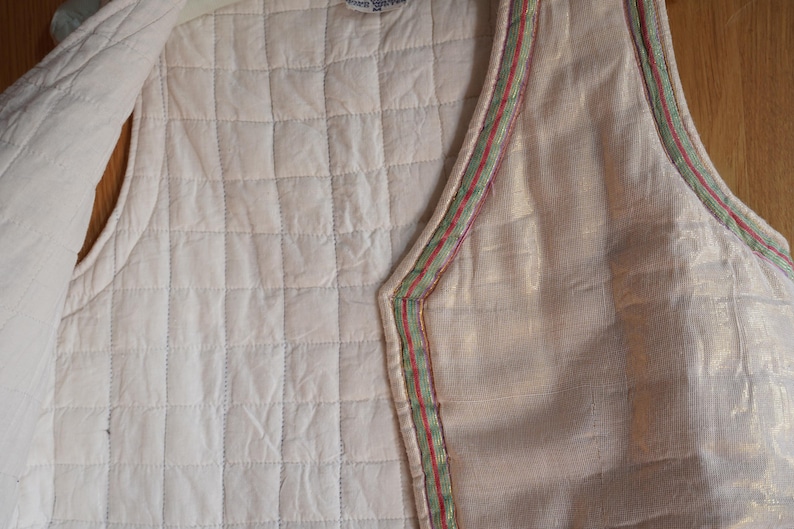 May include: A quilted vest with a white background and a green and red trim. The vest is made of a soft, lightweight fabric and has a relaxed fit.