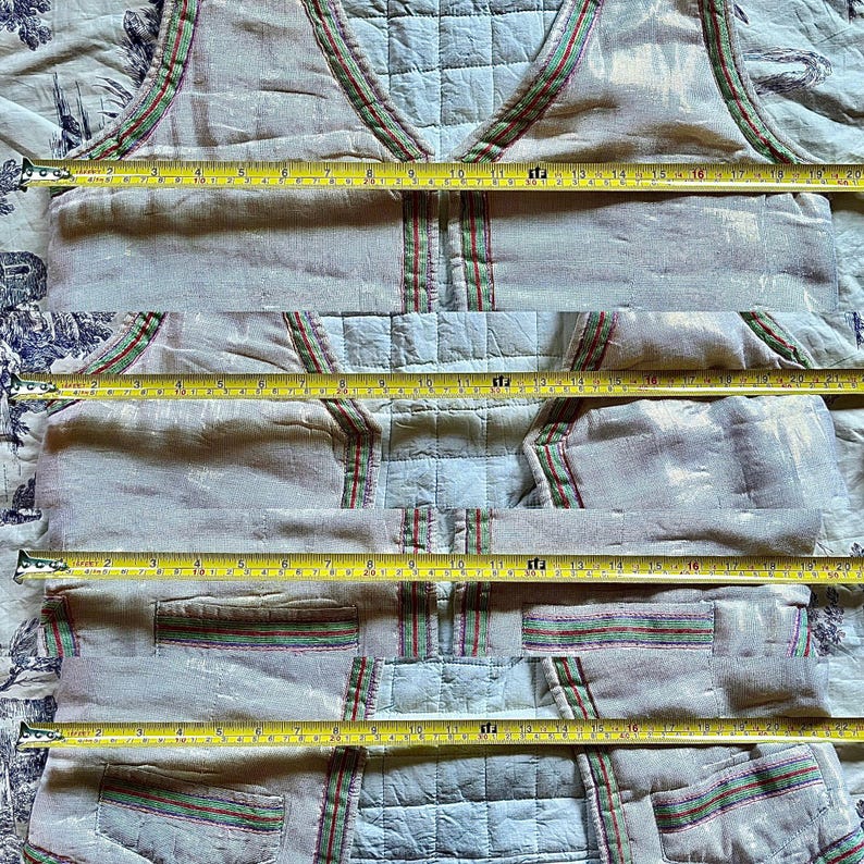 May include: A white vest with a green, red, and white striped trim. The vest has two pockets on the front and is made of a lightweight fabric.