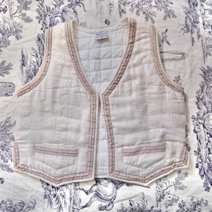 May include: A white quilted vest with a red and green trim. The vest has two pockets and a V-neck.