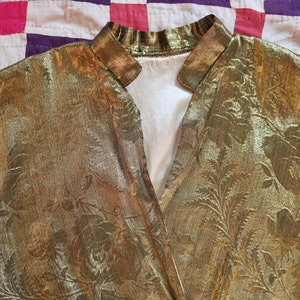 May include: A gold metallic fabric with a floral pattern. The fabric has a sheen and a textured surface.
