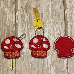 May include: Three red and white mushroom-shaped keychains with white polka dots. The keychains are attached to a gold key with a key ring.