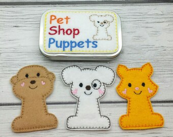 May include: Set of three felt finger puppets in a tin. The puppets are a brown dog, a white dog with a black eye patch, and an orange cat. The tin has the words "Pet Shop Puppets" on it.