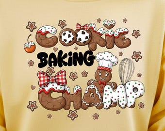 May include: A yellow sweatshirt with a whimsical design featuring the words "Cookie Baking Champ" in a playful, cookie-themed font. The design includes gingerbread men, stars, and cookie accents.
