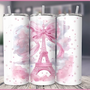 Puede incluir: Un diseño de acuarela rosa y blanco con la Torre Eiffel y un gran lazo rosa. El diseño está en un vaso blanco con una tapa transparente y una pajita.