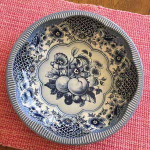 Puede incluir: Un tazón de porcelana azul y blanco con un diseño floral y un motivo de frutas. El tazón tiene un borde festoneado y un borde elevado.