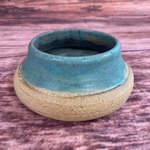 May include: A small, round ceramic planter with a light blue glaze on the top half and a speckled beige glaze on the bottom half.