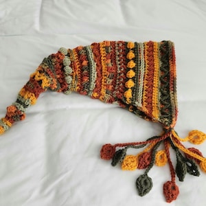 May include: A handmade crochet hat in autumn colors, featuring a long, pointed shape and a tassel of leaf-shaped embellishments. The hat is primarily orange, brown, and green, with textured stitch patterns.