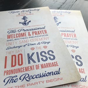May include: Two white wedding fans with blue and red text. The text reads "The Processional", "Welcome & Prayer", "Selected Readings", "Unity Sand Ceremony", "Exchange of Vows & Rings", "They Say", "I Do Kiss", "Pronouncement of Marriage", "The Recessional", "Let the Party Begin!" and "Seating of the Parents".