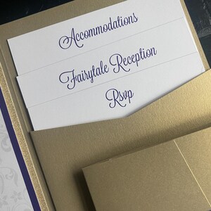 May include: A gold wedding invitation suite with inserts. The inserts have the words "Accommodations", "Fairytale Reception", and "RSVP" in a dark blue script font. The invitation has a purple and gold border.
