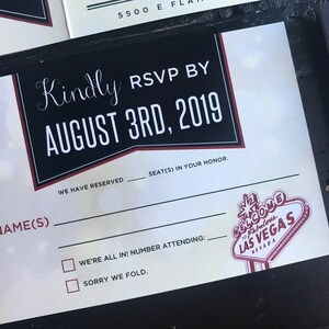 May include: A black and white RSVP card with red accents. The card has a black and white graphic of the Las Vegas sign. The text on the card reads "Kindly RSVP by August 3rd, 2019".