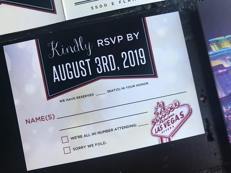 May include: A black and white RSVP card with red accents. The card has a black and white graphic of the Las Vegas sign. The text on the card reads "Kindly RSVP by August 3rd, 2019".