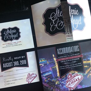 May include: Wedding invitation suite with a black and white design featuring the names "Stefenie & Angel" and a red and white "Welcome to Fabulous Las Vegas" sign. The invitation includes details about the wedding location, date, and RSVP information.