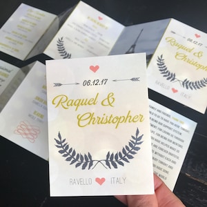 Puede incluir: Una invitación de boda con fondo blanco y texto dorado. La invitación dice "06.12.17 Raquel & Christopher Ravello Italia". La invitación está decorada con una corona de hojas y un corazón.