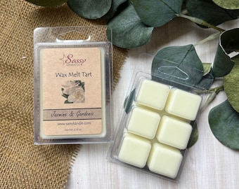 May include: Two wax melt tarts in clear plastic packaging. One package features a brown label with the text "Sassy Kandle Co" and "Jasmine & Gardenia." The other package contains six pale yellow wax cubes. The net weight is 2.75 oz.