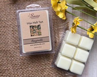 May include: A six-pack of wax melts in a clear plastic container. The wax melts are white and have a floral scent. The label on the container reads "Sassy Candle Co. Wax Melt Tart Honeysuckle www.sassycandle.com Net Wt. 2.75 oz."