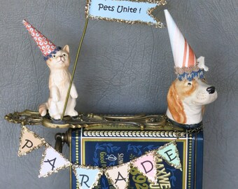 Parade dog and cat whimsical assemblage sculpture.  Cat is riding atop a dog proudly proclaiming "Pets Unite!"