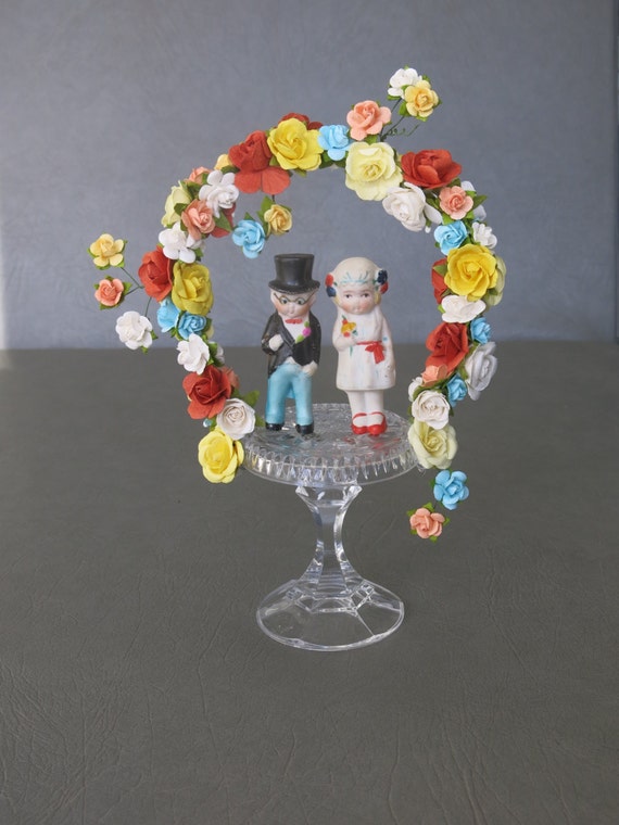 Wedding or Anniversary cake topper.  Bisque 1920s bride and groom set atop cut crystal base adorned with an arch of colorful paper flowers.