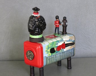 Assemblage poodle.  One of a kind. "British Bobby."  Black porcelain poodle with British tin with Queen's guards graphics and lead soldier.