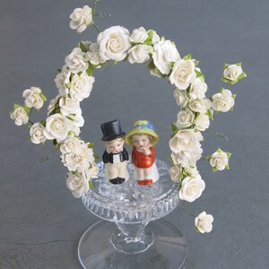 Wedding or Anniversary cake topper. Vintage porcelain bride and groom set atop cut crystal base and arch of white paper flowers. image 3