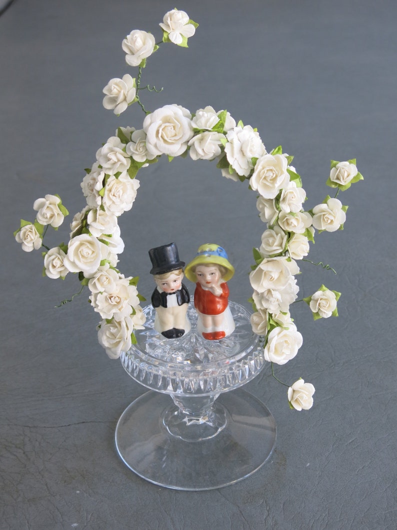 Wedding or Anniversary cake topper. Vintage porcelain bride and groom set atop cut crystal base and arch of white paper flowers. image 3