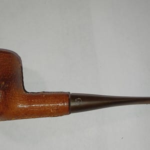 May include: A brown tobacco pipe with a rounded bowl and a long, slender stem. The bowl has a textured, leather-like appearance, while the stem is a darker brown. The pipe is designed for smoking tobacco.