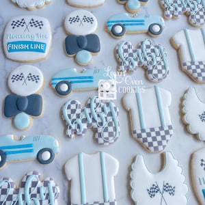 Puede incluir: Una colección de galletas decoradas con temática de carreras que incluye coches de carreras azul claro, baberos blancos con banderas a cuadros, bodies con tirantes y galletas con el texto Nearing the Finish Line y Baby.