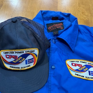 May include: A blue jacket with a patch that reads "Computer Power Systems CPS Racing Team Emerson Electric". A blue and black mesh baseball cap with the same patch is also pictured.