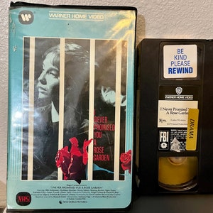 May include: A VHS tape of the movie "I Never Promised You a Rose Garden" with a blue and white cover featuring a woman with short hair and a red rose. The tape is labeled "Warner Home Video" and has a "Be Kind Please Rewind" sticker on it.