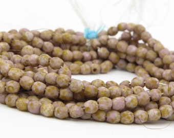 May include: Strands of light purple and gold-toned beads. The beads have a faceted, textured surface and are strung together. The beads are bunched together, with a white background. The beads are tied together with a blue string.