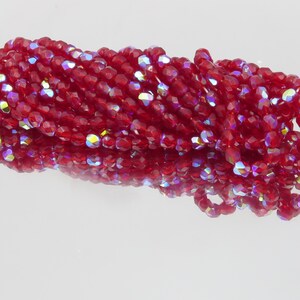 Può includere: Un fascio di perline rosse scure sfaccettate con riflessi iridescenti. Le perline sono infilate insieme, riflettendo la luce e creando un effetto scintillante. Ideale per la creazione di gioielli o progetti artigianali.