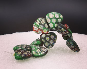 May include: A collection of green, red, and silver artisan beads. The beads have a unique, textured design with a mix of colors and patterns. The beads are strung together, showcasing their individual shapes and details.