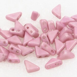 May include: A collection of light pink triangle and rectangular shaped beads. The beads have two holes for stringing. The beads are scattered across a white surface. These beads are ideal for jewelry making and crafting.