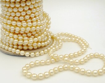 May include: A spool of cream-colored faux pearls, with a strand of pearls unraveled. The pearls are round and evenly sized, creating a classic and elegant look. Ideal for jewelry making or craft projects.