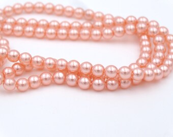 May include: Strands of peach-colored faux pearls against a white background. The pearls are round and evenly sized, with a subtle sheen. The image shows multiple strands, suggesting they are ready for jewelry making or crafting.