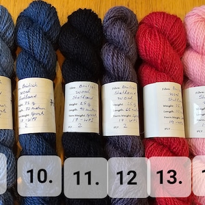 May include: Six skeins of British Shetland wool yarn in various colors: light blue, dark blue, black, purple, red, and pink. Each skein is labeled with weight and length information. Ideal for knitting and crochet projects.