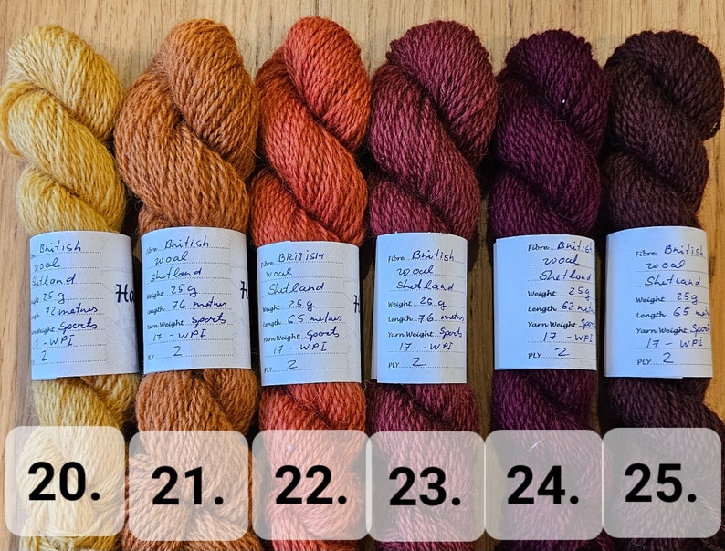 May include: Six skeins of British Shetland wool yarn in a range of warm colors, from golden yellow to deep burgundy. Each skein is labeled with weight, length, and yarn weight details. The numbers 20 through 25 are visible at the bottom.