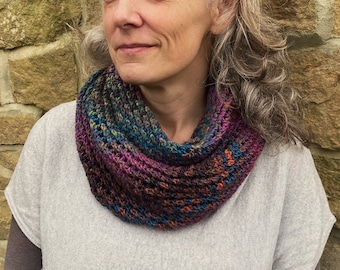 Puede incluir: Una mujer con cabello gris que lleva una bufanda infinita de punto de colores. La bufanda está hecha con una variedad de colores, incluyendo morado, azul, verde y naranja.