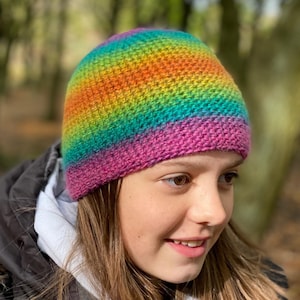 May include: A rainbow striped crocheted beanie hat with a pink brim. The hat is made with a textured stitch.
