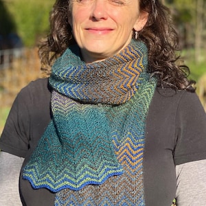 Puede incluir: Una mujer con una camisa negra y una bufanda de color verde azulado, marrón, azul y naranja con un patrón de chevron.