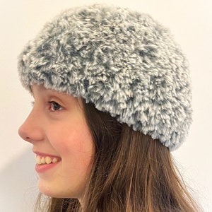 Op de afbeelding: Een grijze beanie van imitatiebont met een zachte, pluche textuur.
