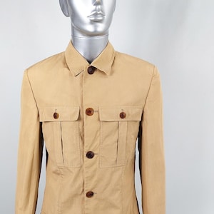 May include: A long-sleeved, tan utility jacket with a button-up front and multiple pockets. The jacket has a relaxed fit and a collar.