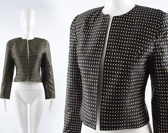 May include: A black cropped jacket with a gold polka dot pattern. The jacket has a zipper closure and long sleeves.