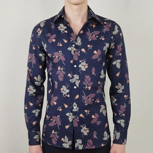 Pode incluir: Camisa azul marinho de manga comprida com um padrão floral. O padrão inclui folhas e flores em tons de roxo, pêssego e verde. A camisa tem uma gola clássica e punhos abotoados.