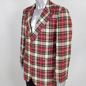 May include: A blazer featuring a red, cream, black, and yellow plaid pattern. The garment has a notched lapel, long sleeves, and two buttons on the front closure. The fabric displays a classic tartan-style check design throughout the exterior.