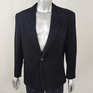May include: A black blazer with a single-button closure, displayed on a mannequin. The blazer has a notched lapel, a chest pocket, and two front pockets. The mannequin is wearing navy blue pants.