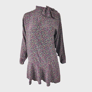 May include: A long-sleeved, gray dress with a bow at the neck. The dress has a small, colorful print of abstract shapes.