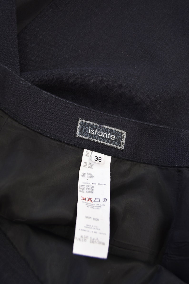 Puede incluir: Una falda negra con una etiqueta blanca que dice "Istante Versace" y tiene la talla 38. La etiqueta tambi&eacute;n incluye la composici&oacute;n del tejido: 70% seda, 30% lana, 70% seda, 30% lana, 100% ray&oacute;n, 100% ray&oacute;n, 100% ray&oacute;n. La etiqueta tambi&eacute;n incluye instrucciones de cuidado: limpieza en seco profesional, no blanquear, no secar en secadora, planchar en caliente.