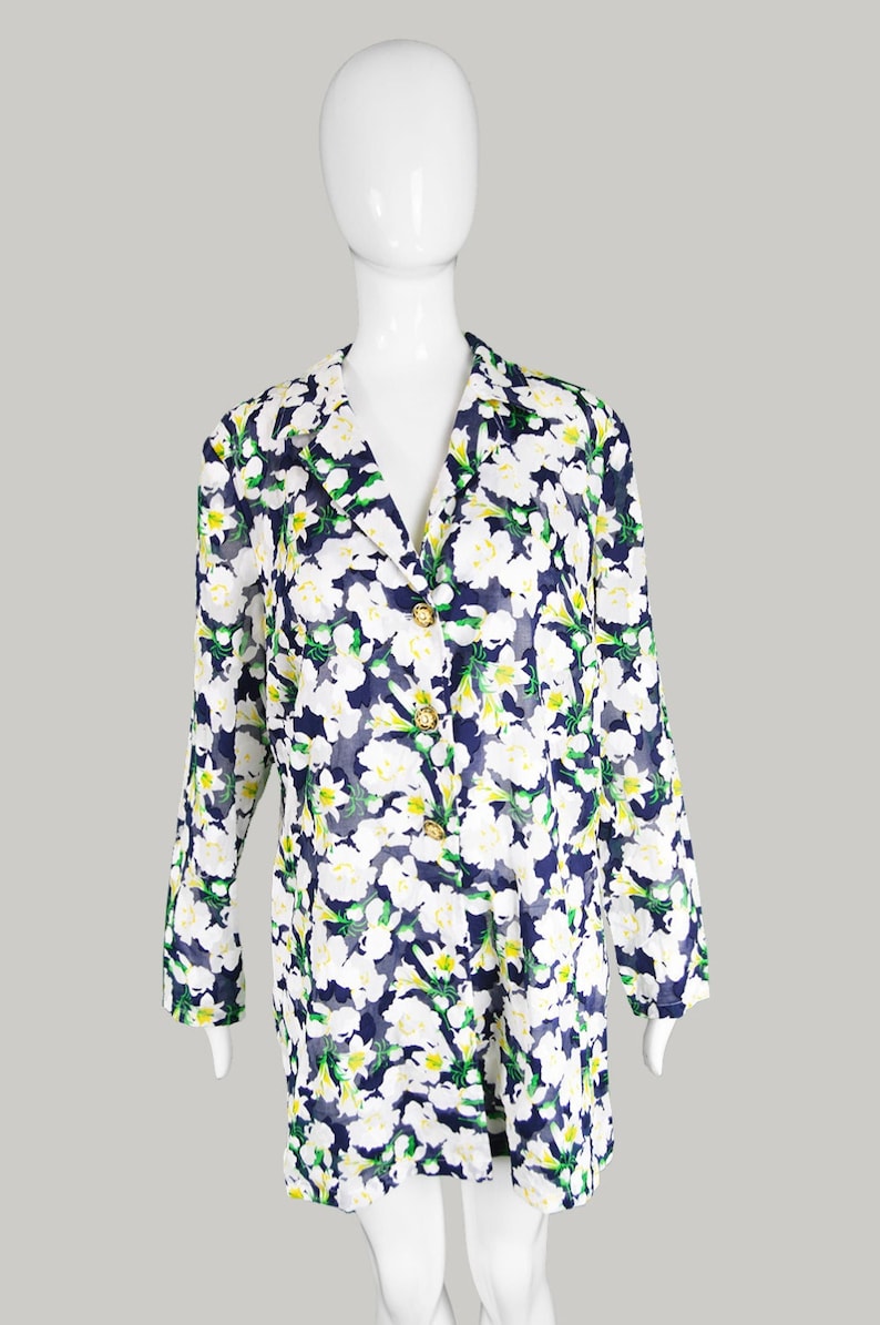 Pu&ograve; includere: Una camicia bianca a maniche lunghe con bottoni e stampa floreale in tonalit&agrave; di verde, bianco e blu. La camicia ha un collo a V e bottoni dorati.