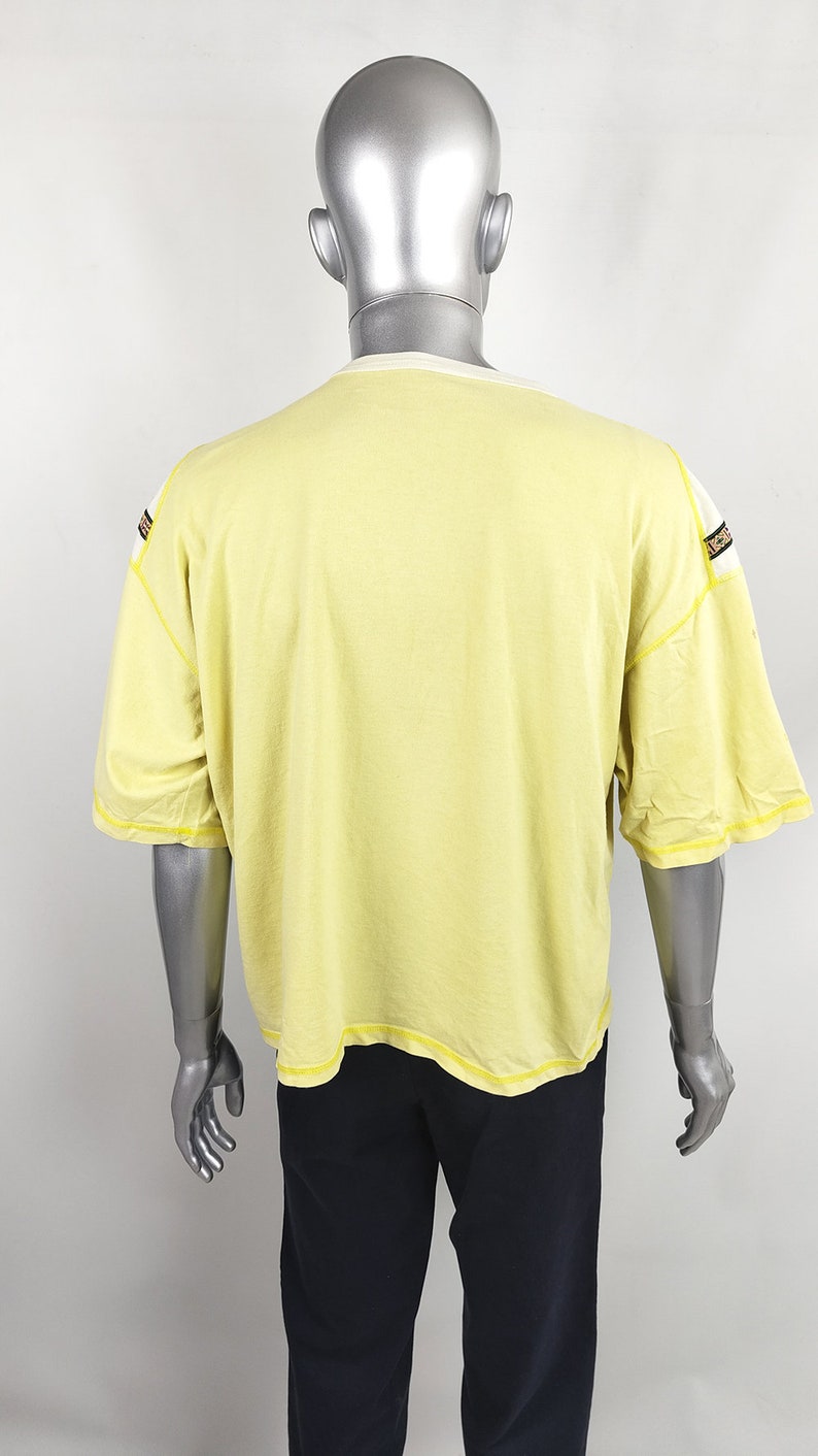 May include: A yellow short-sleeved t-shirt with black and white trim on the shoulders and sleeves. The t-shirt is on a mannequin.